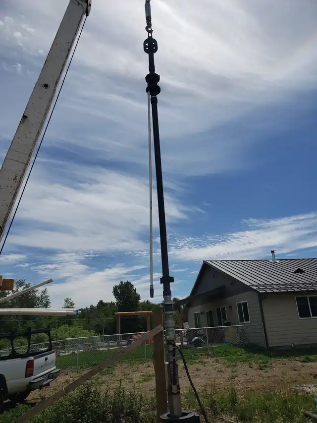 A long pump column hanging from Akland's crane mast beside a house, a pickup parked below
