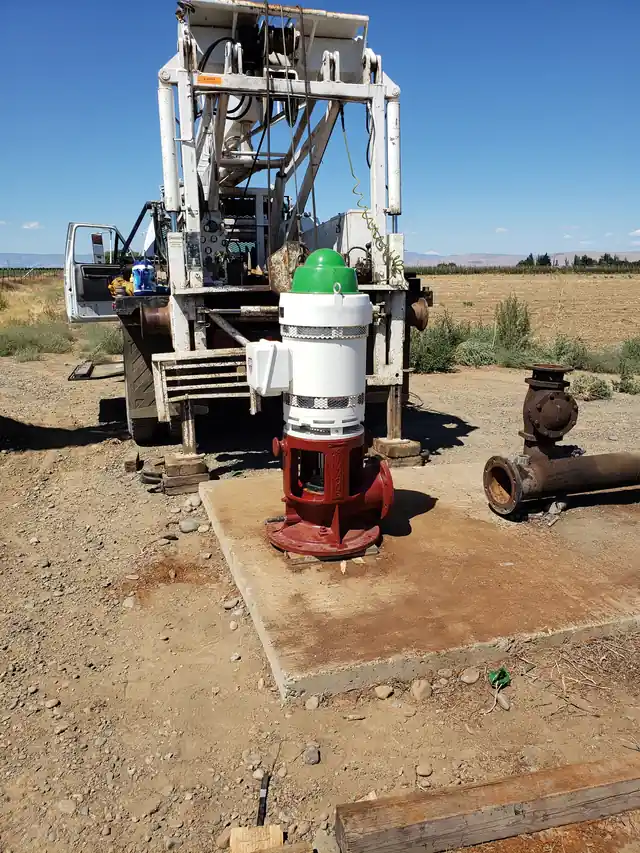 Akland's pump rig setting a vertical turbine motor onto a red pump head on a concrete pad