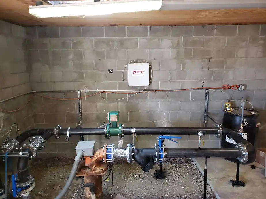A pump room against a block wall with a black manifold, meters and blue valves