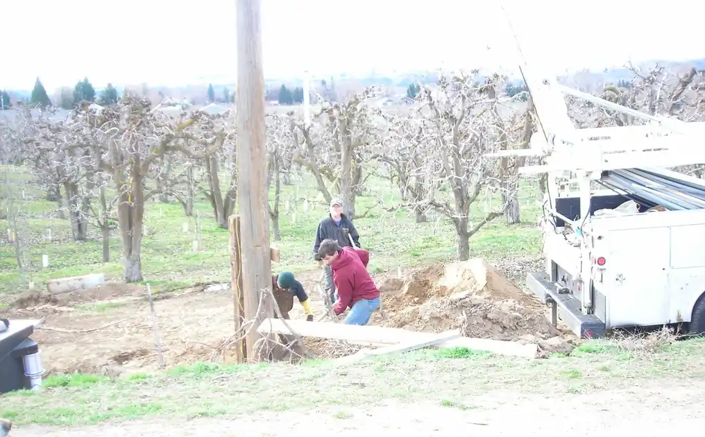 Akland crew working at a well in a bare winter orchard, the crane service truck parked beside them