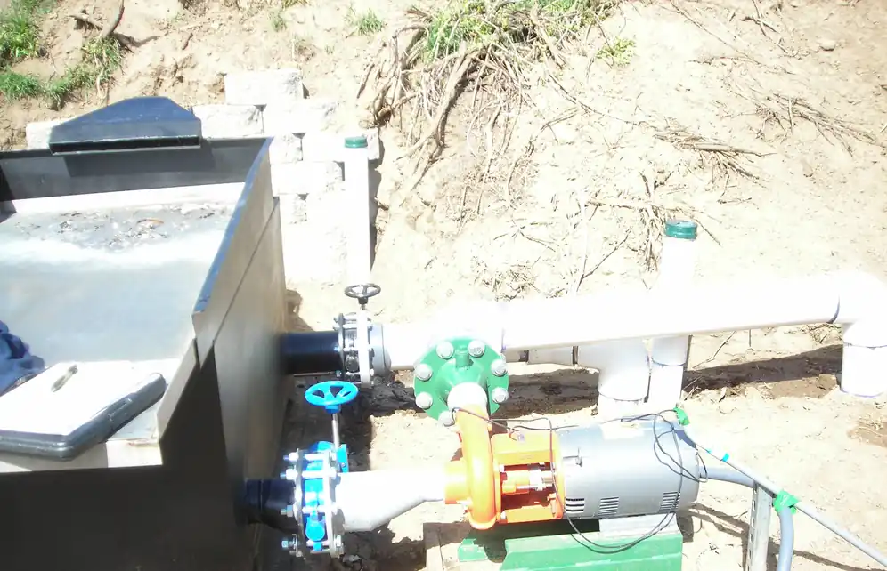 A new centrifugal irrigation pump plumbed to a steel intake box on a dirt bank