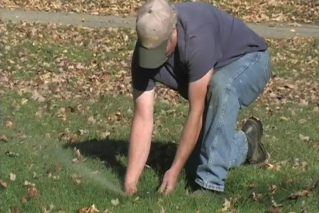 A technician close to a sprinkler head on a lawn, adjusting it