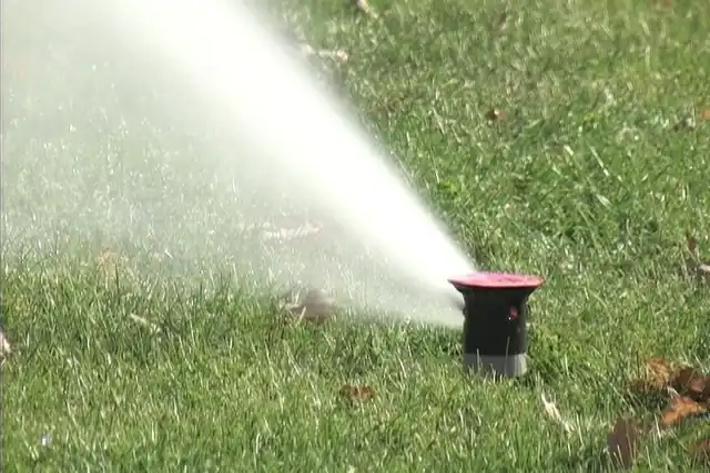 A rotor sprinkler throwing water across a green lawn