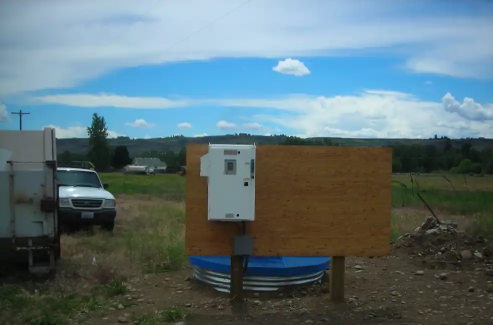 A variable frequency drive panel on a steel stand over a well, with an open field behind